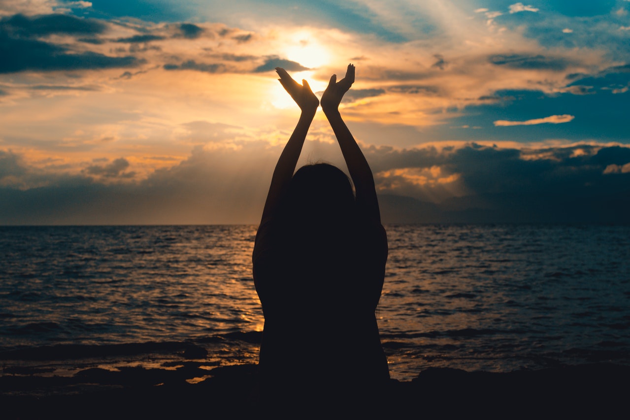 Person Raising Hands Near Sea at Sunset