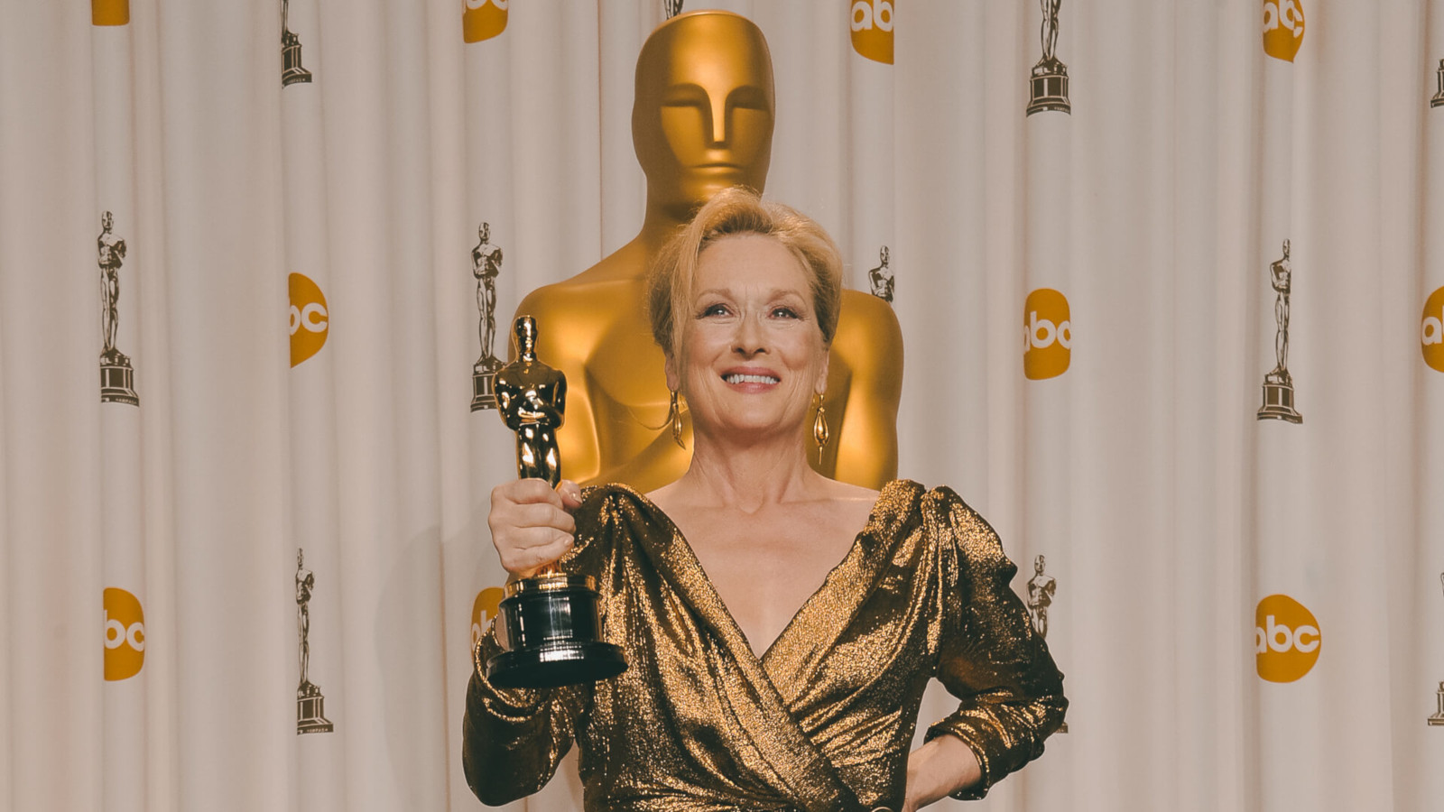 Meryl Streep wearing gold dress while holding a trophy