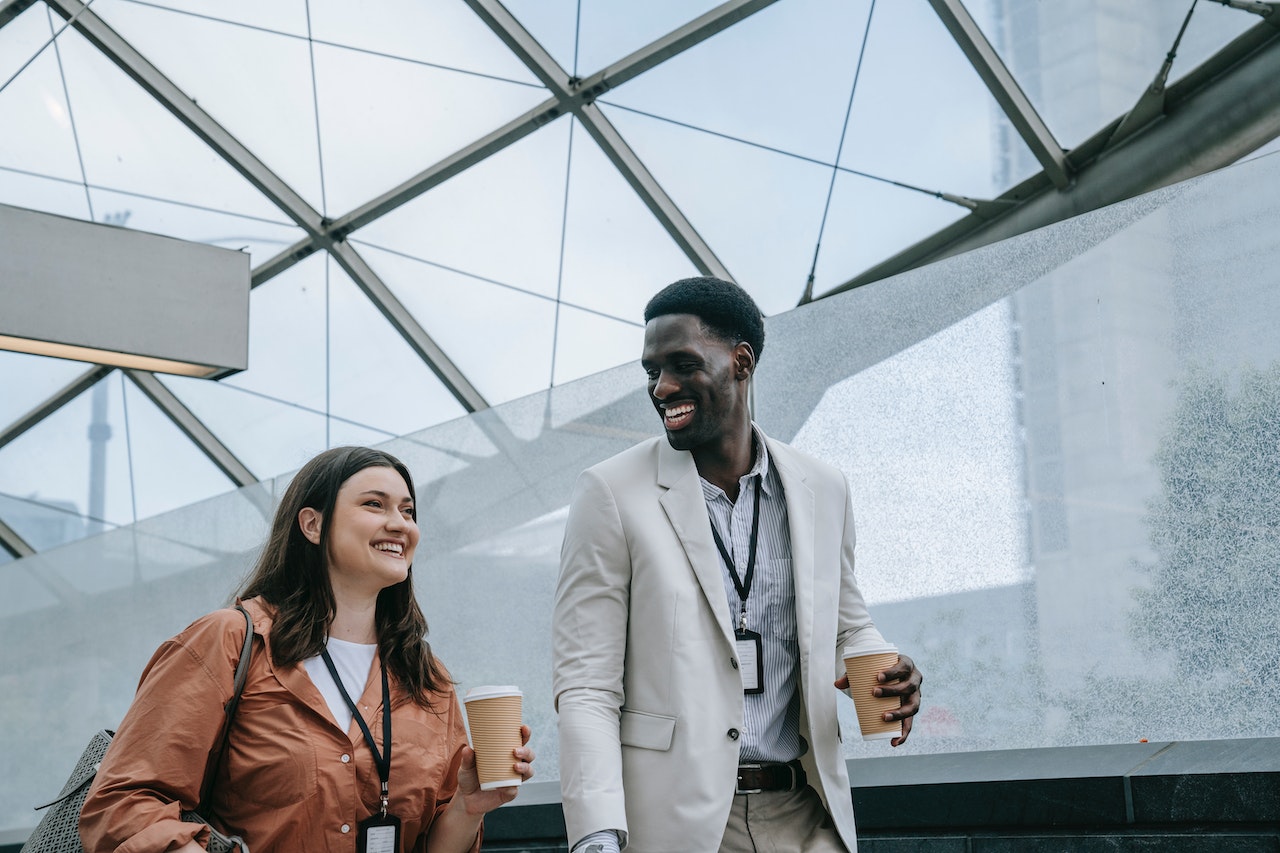 A Couple Walking Holding Their Coffee And With Big Smiles On Their Faces