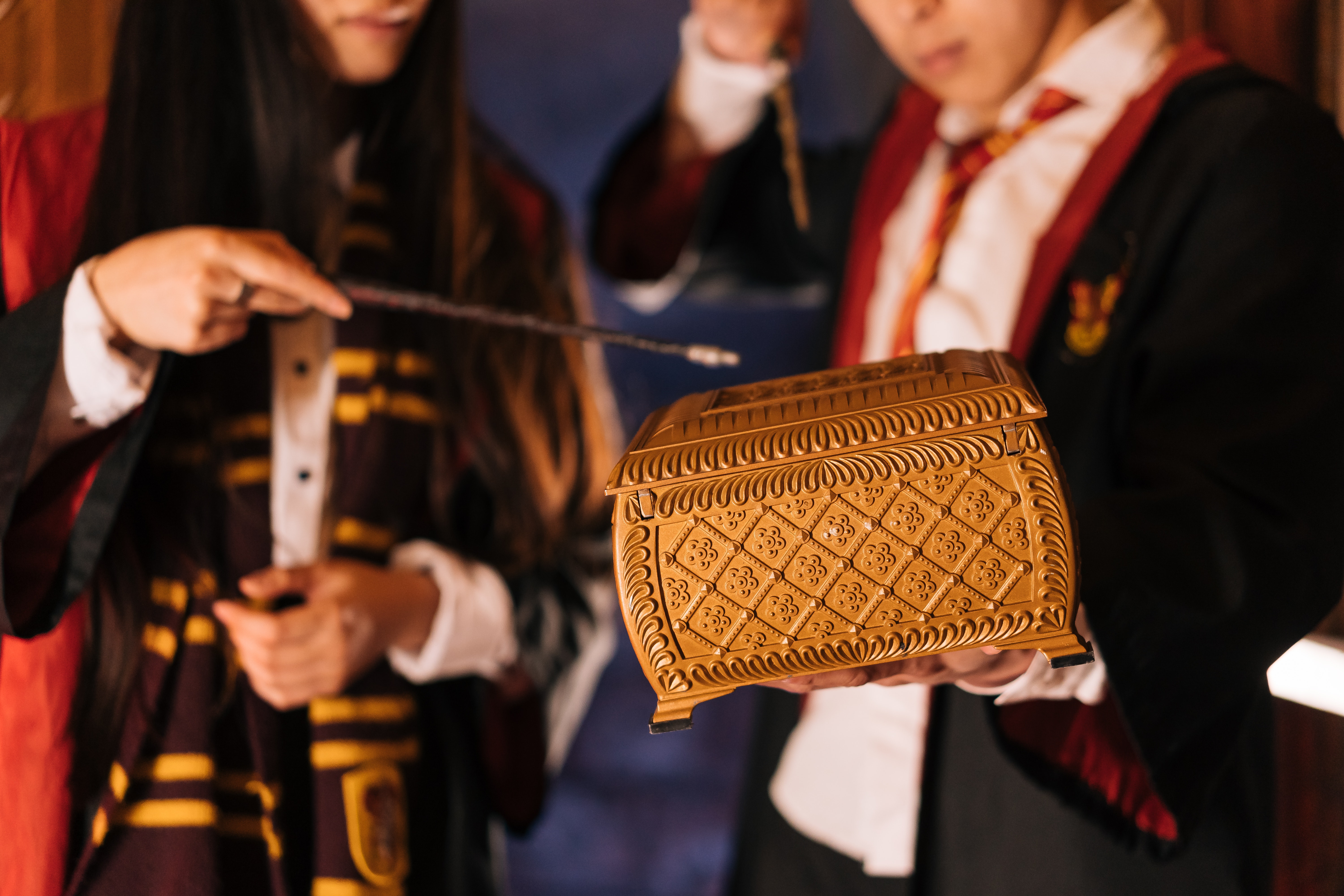 A girl and a boy holding a wand over a brown box.