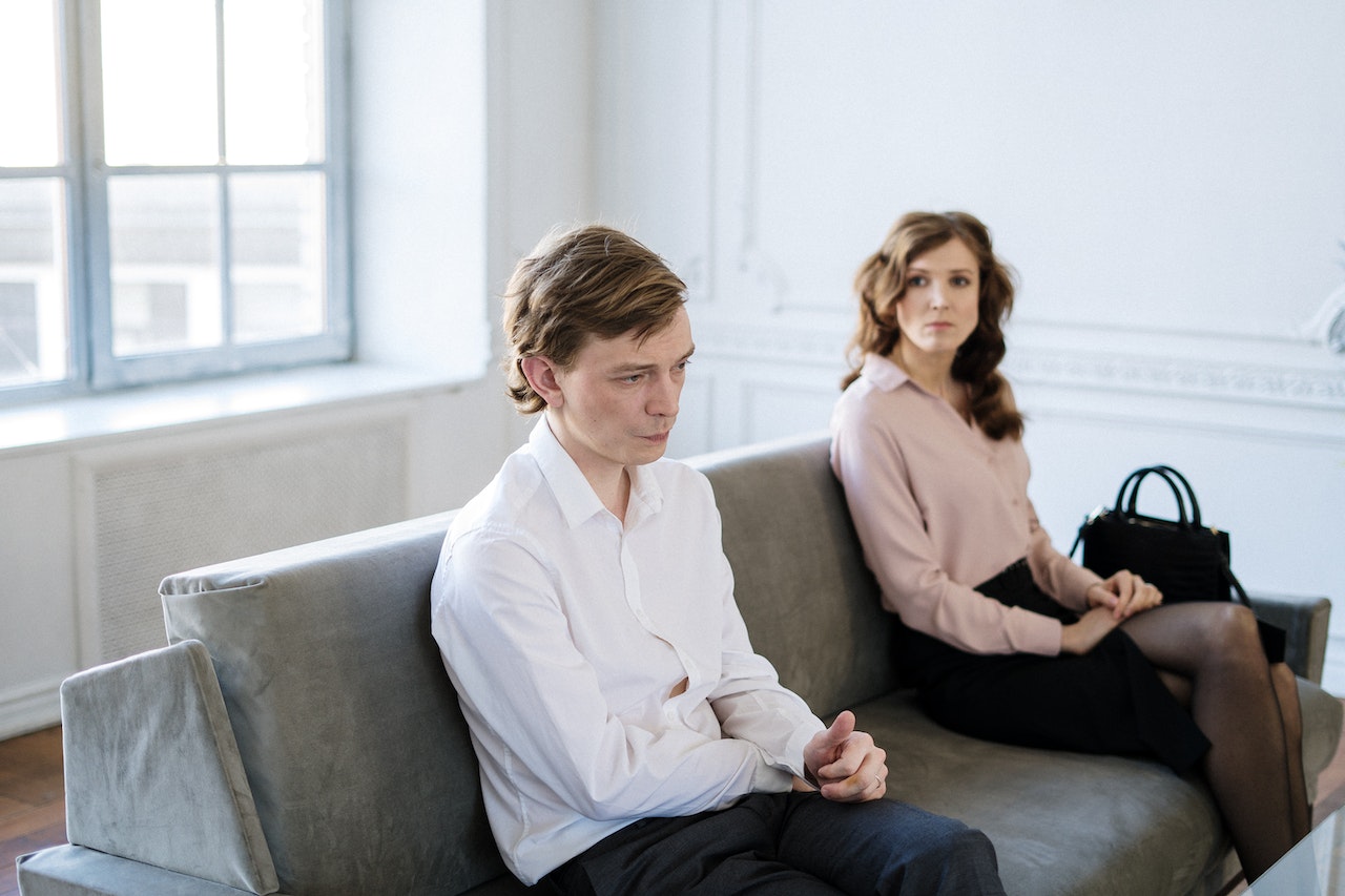Man in White Suit Sitting Beside Woman in Black Dress